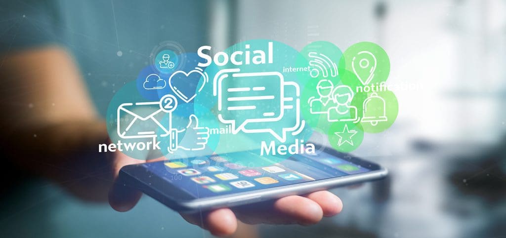 A person holding an iPhone in their hand with an illustrated image of social media networks, likes, hearts, and notifications on top of it.