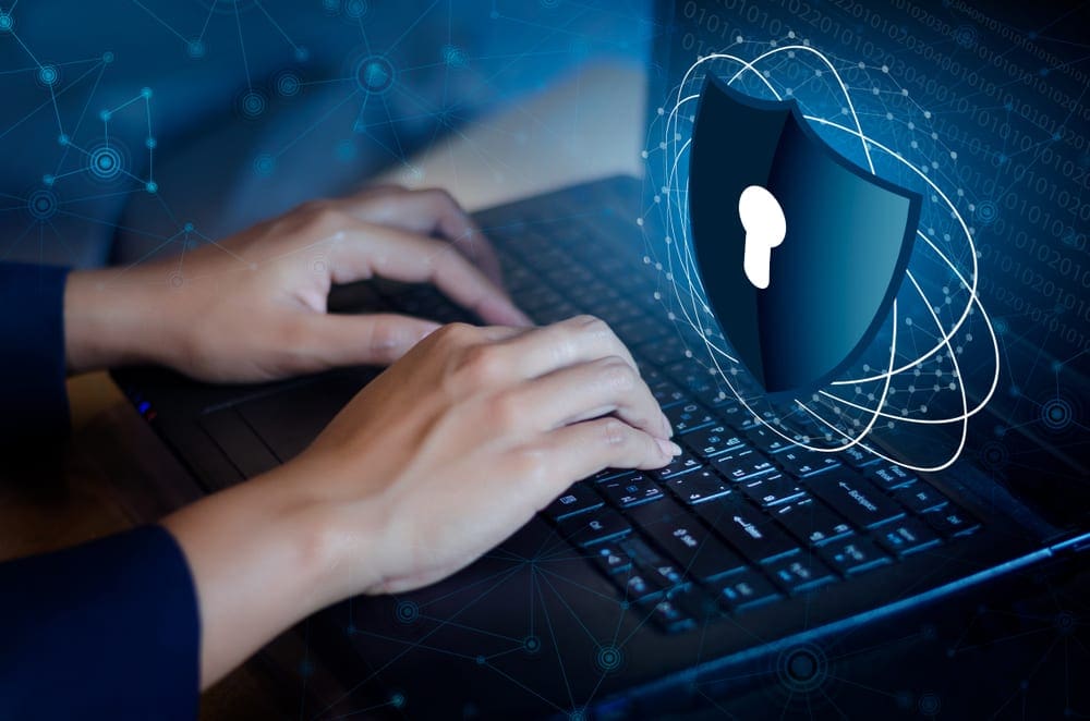 Hands typing on a laptop keyboard with a cybersecurity shield on the screen.