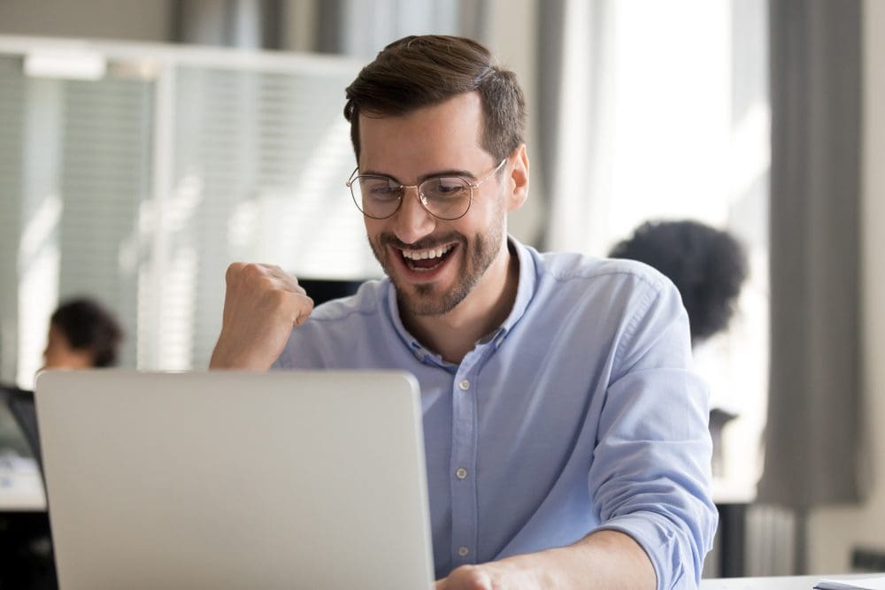 A happy man looking at his laptop in a business environment is excited his data was recovered successfully