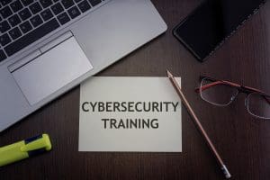 A desk with a laptop, highlighter, pencil, glasses, and a note that says “Cybersecurity Training"