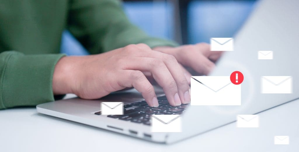 A man using a laptop with many email images superimposed, one of which with an alert.