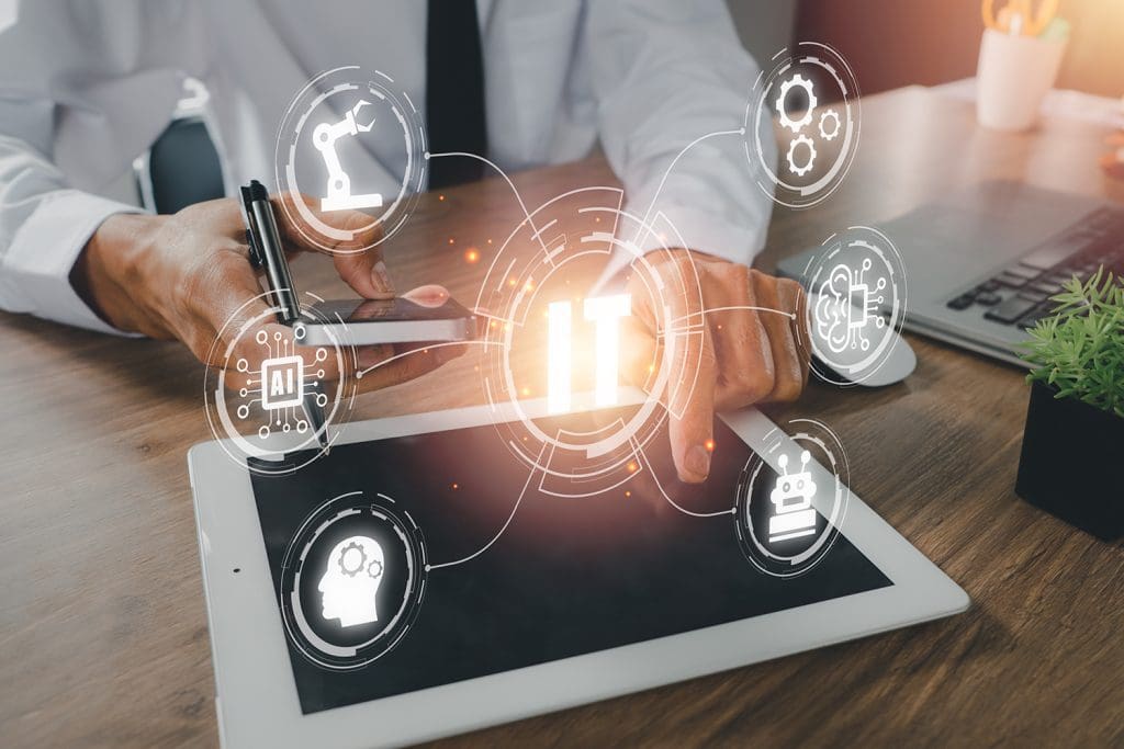 A man at a desk, in a white dress shirt, using multiple devices with IT-concept images appearing above a tablet.